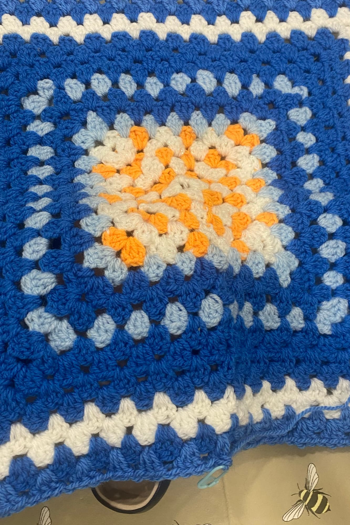 A finished granny-square cushion cover in blue, white and orange, made at crochet club.