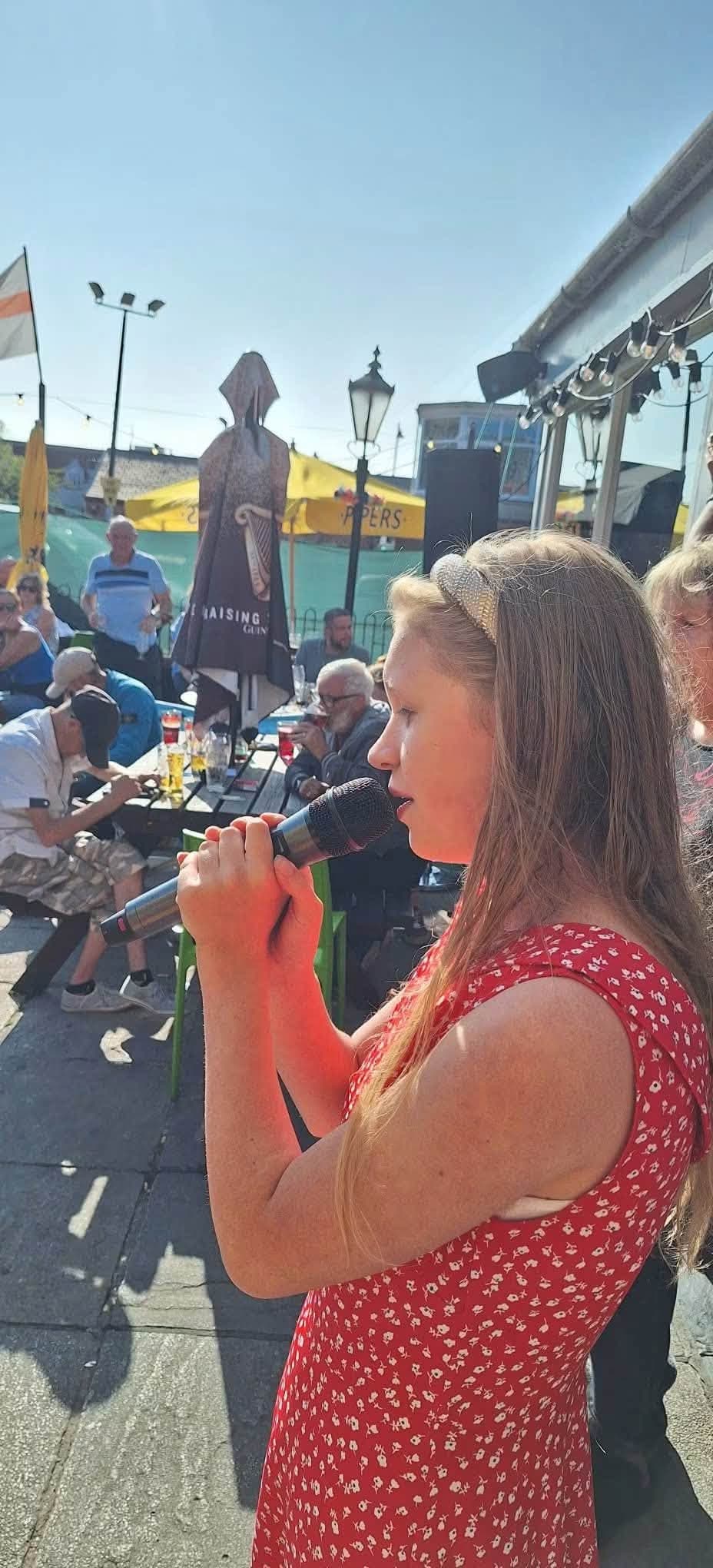 A young singer performing on the microphone in the beer garden.