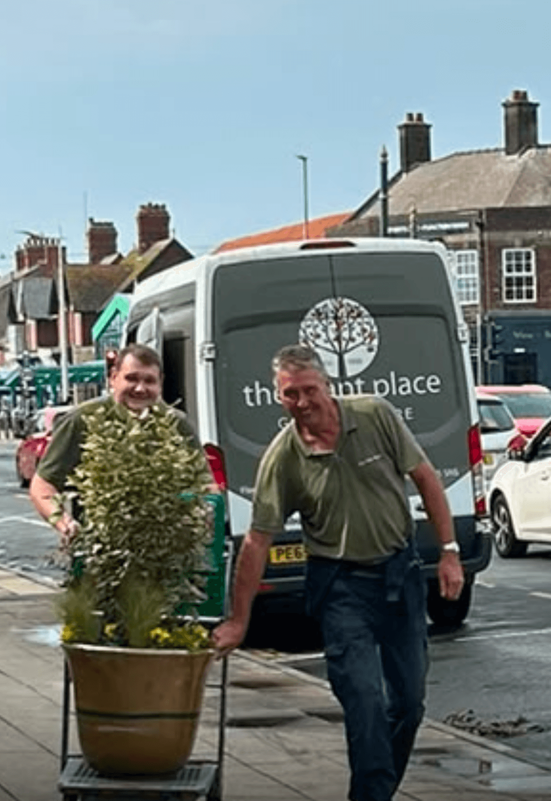 Two men from The Plant Place wheeling a planted pot along the parade from their van.