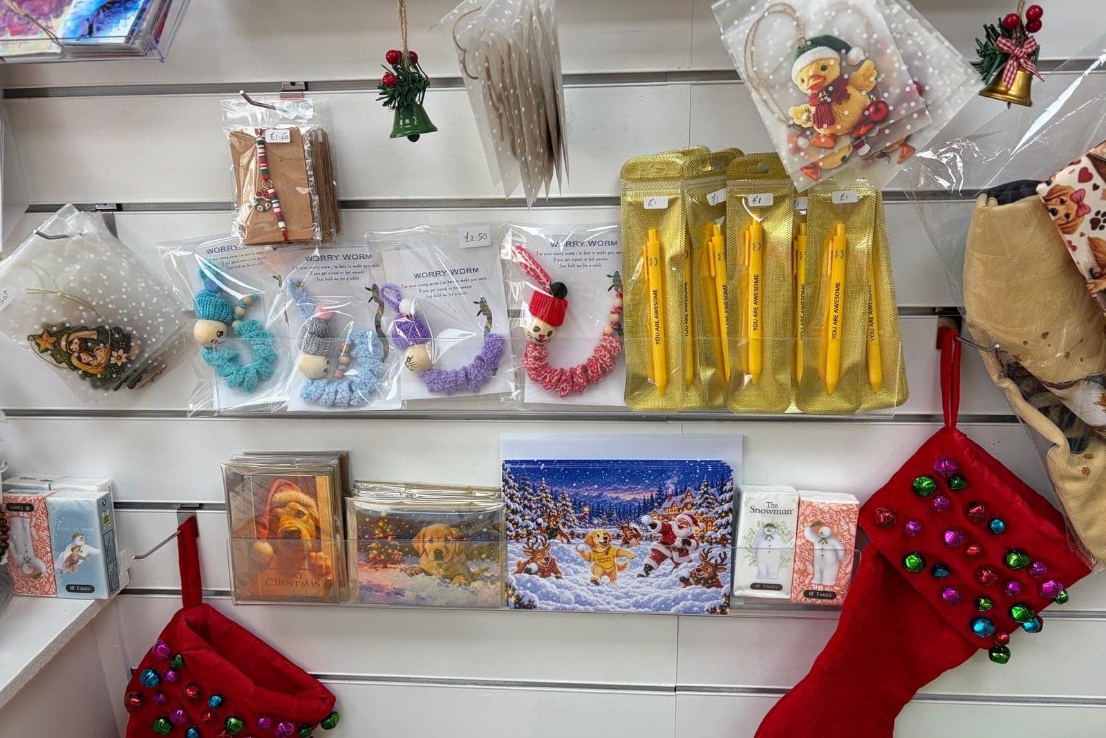 Handmade worry worms, cards and gifts on the gift shop shelves, with Christmas stockings hanging below.