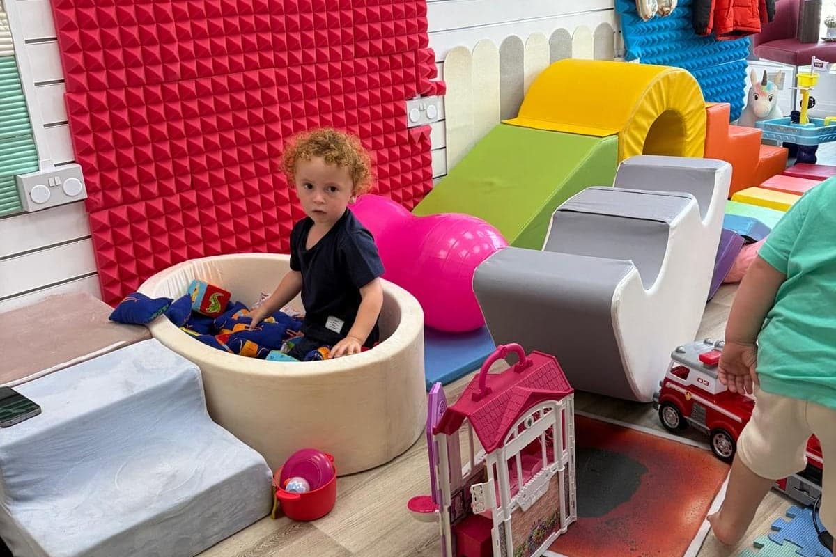 A child playing in the ball pit at the Hub 3 soft play, with foam steps, a slide and toys around them.