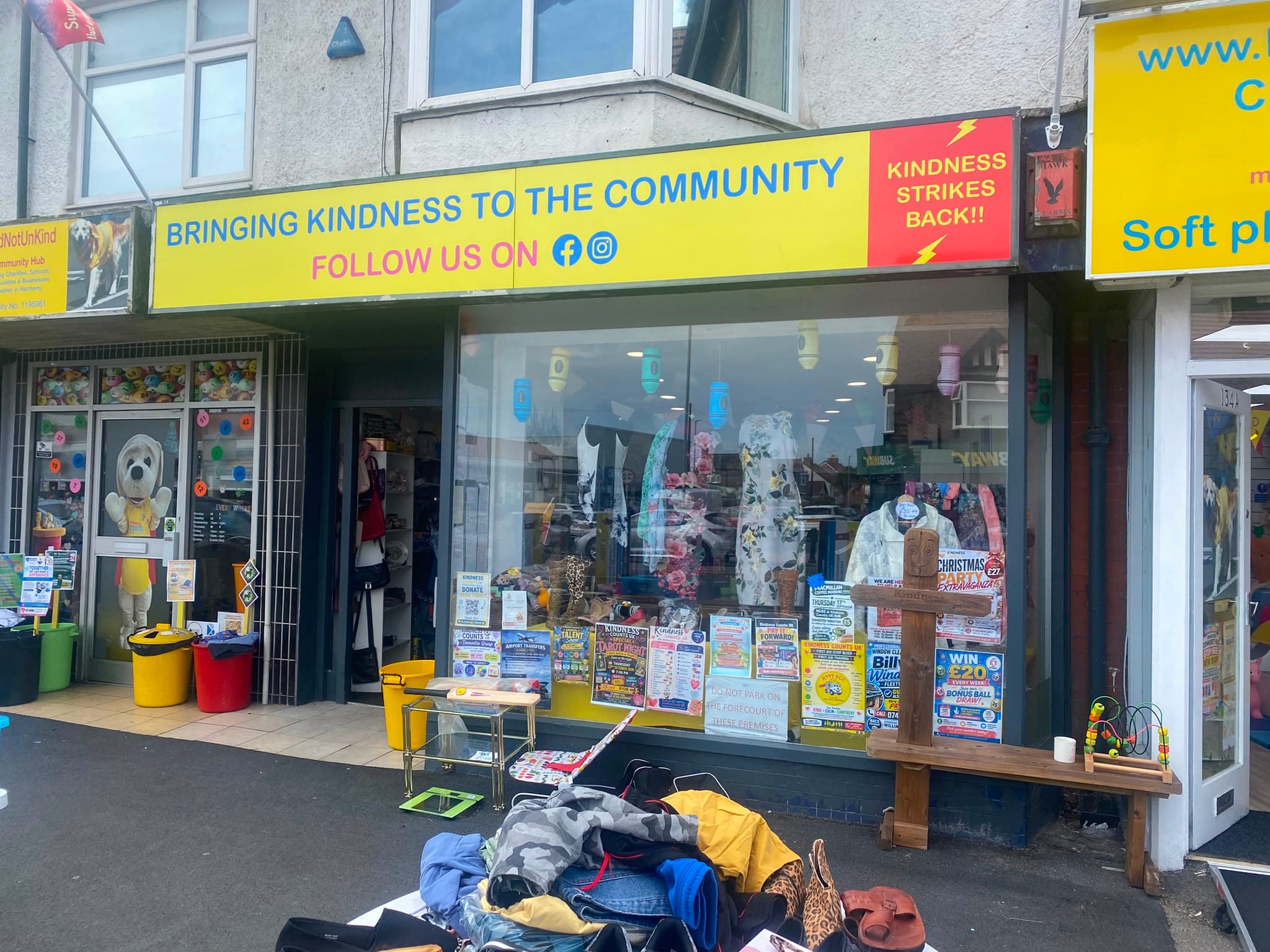 The charity shop on Victoria Road West, under a yellow sign reading 'Bringing kindness to the community'.