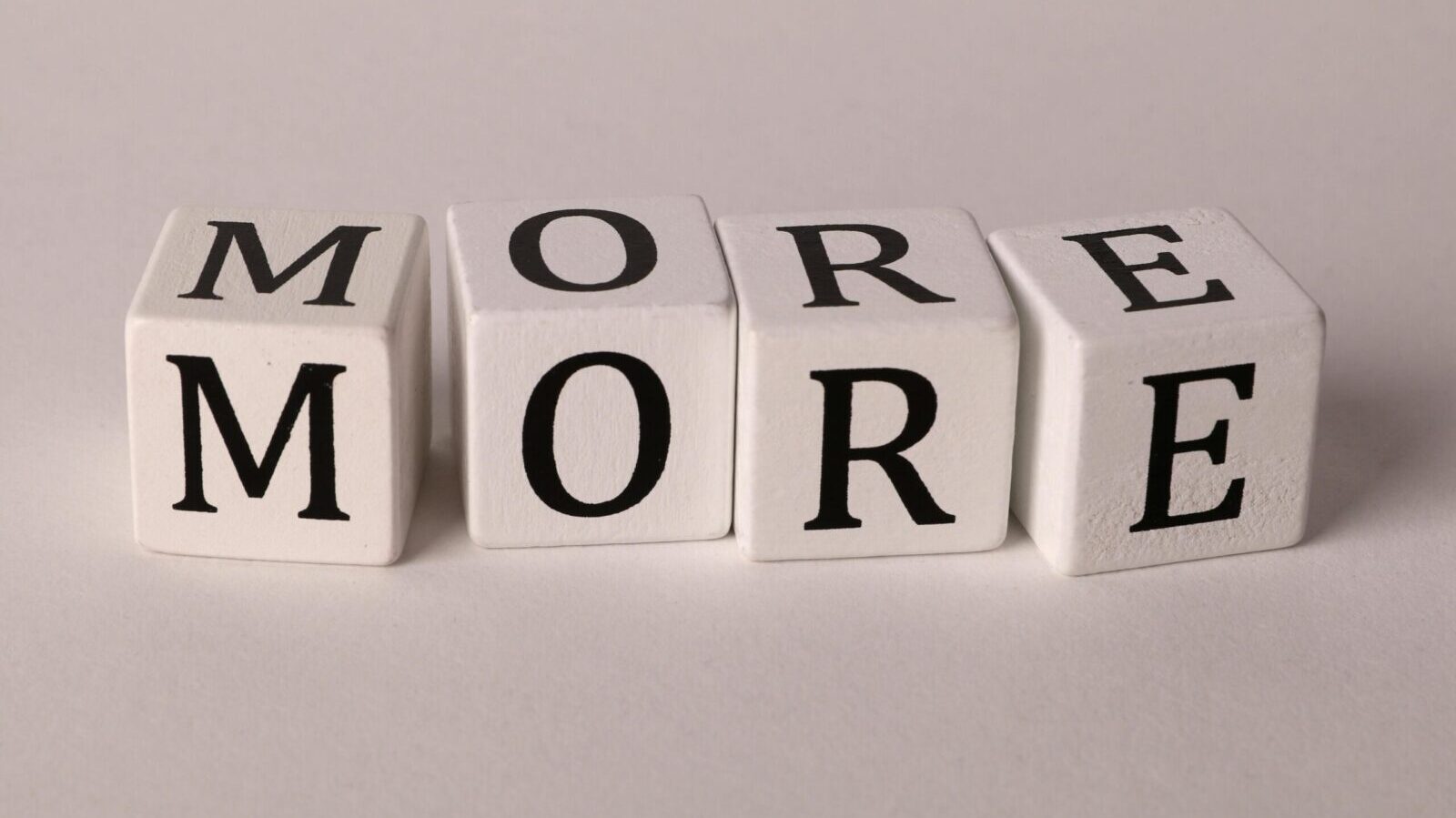 Close-up view of four dice with letters spelling MORE on a white background.
